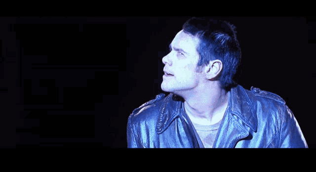 a man in a leather jacket is singing into a microphone in the dark