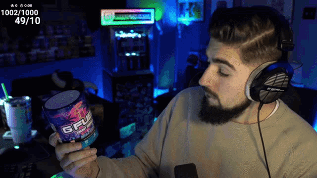 a man wearing headphones holds up a bottle of gfuel
