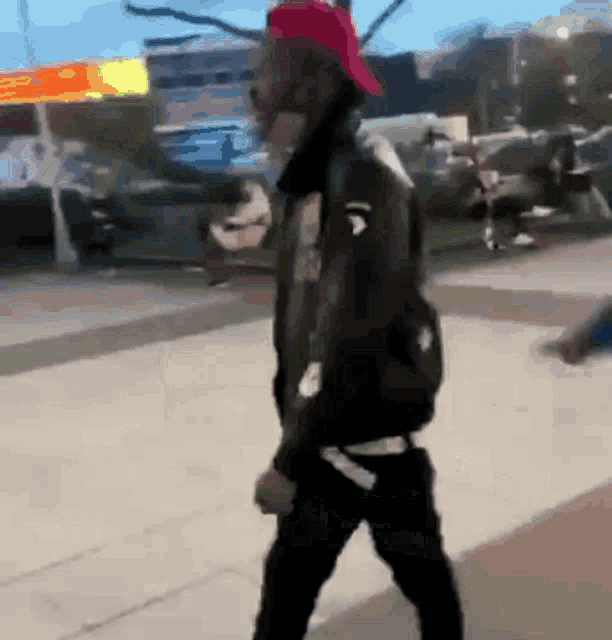 a man wearing a black jacket and a red hat is walking down the street