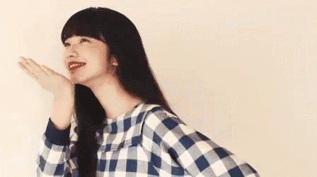 a woman wearing a blue and white plaid shirt is smiling and holding her hand to her face .