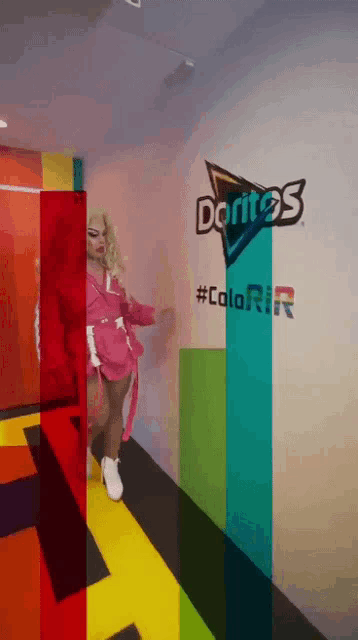 a woman in a pink dress is standing in front of a wall that says doritos