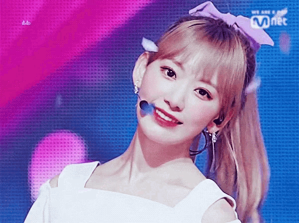 a girl with a ponytail and a bow in her hair stands in front of a sign that says mnet