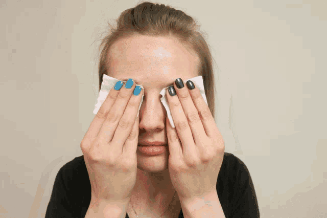 a woman with blue and black nails wipes her eyes with a cloth