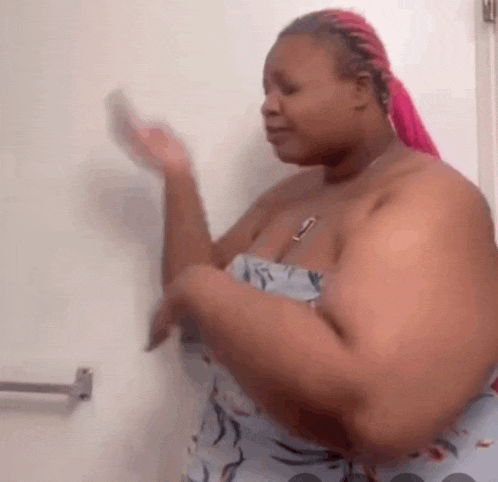 a woman with pink hair is standing in front of a white wall and waving her hands .