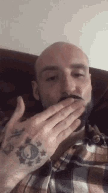 a man with a beard is covering his mouth with his hands .