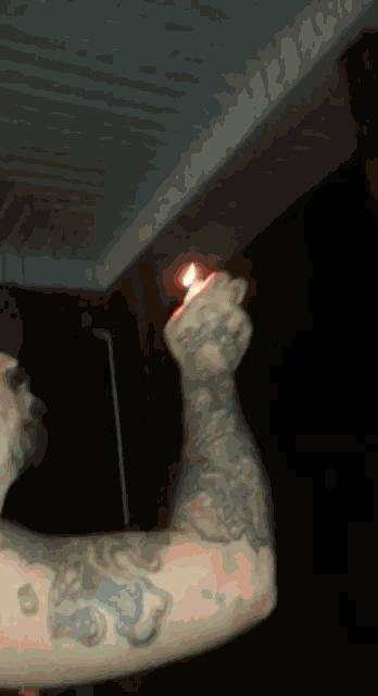 a man with a tattoo on his arm is lighting a lighter