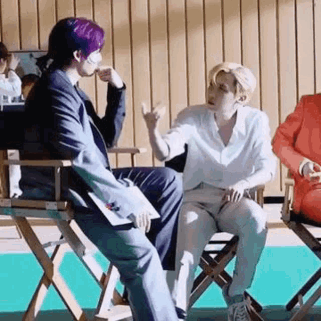 a man in a suit is sitting in a director 's chair talking to another man .