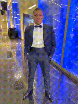 a man in a suit and bow tie is standing with his hands in his pockets .