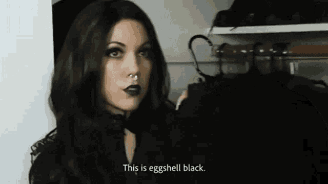 a woman with black hair and black lipstick is standing in a closet holding a black item .