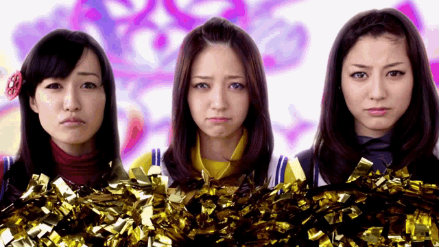 three cheerleaders standing next to each other with gold pom poms in front of them
