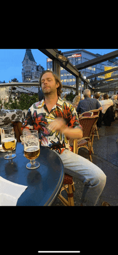 a man in a colorful shirt sits at a table holding a glass of beer