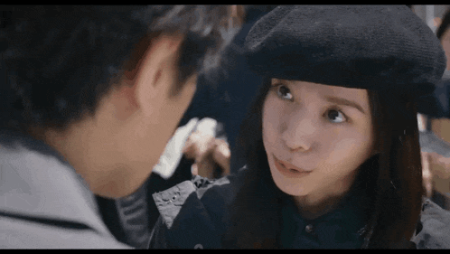 a man and a woman are looking at each other and the woman is wearing a beret .