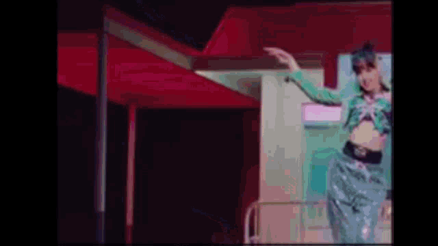 a woman in a green jacket and blue pants is dancing on a stage in front of a red roof .