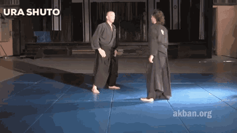 two men are standing on a blue mat and the words ura shuto are on the bottom