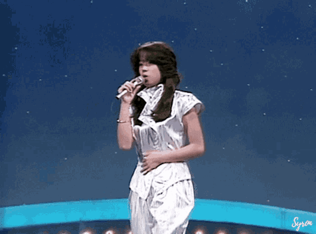 a woman in a silver top is singing into a microphone on stage .