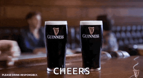 two guinness glasses are sitting on a bar with cheers written in the corner
