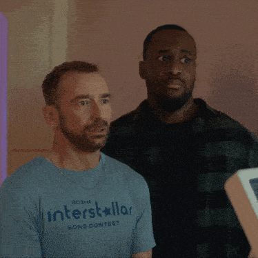 a man wearing an interstellar song contest shirt points at another man