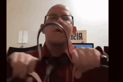 a man wearing glasses and a red shirt is holding a pair of headphones in front of his face .