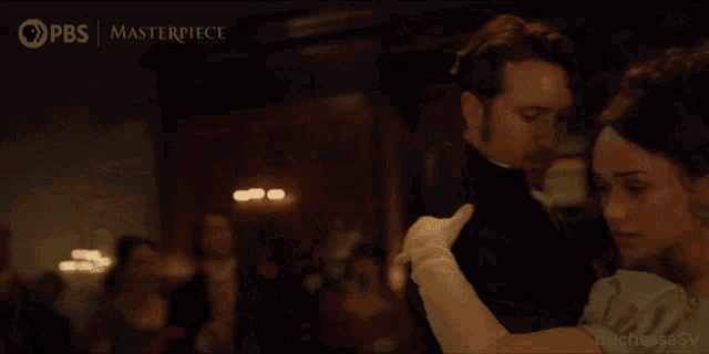 a man and a woman are dancing in front of a pbs masterpiece logo