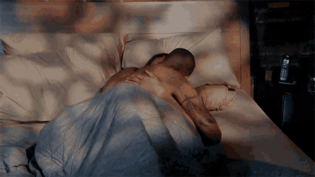 a man and a woman are laying in bed with a phone on the nightstand