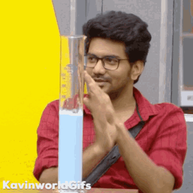 a man wearing glasses is clapping in front of a beaker of blue liquid