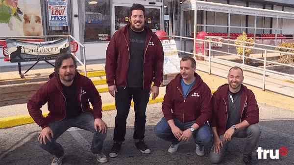 four men are posing for a picture in front of a store with a sign that says " low prices "