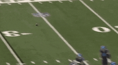 a football player is laying on the ground on a field while a referee watches .
