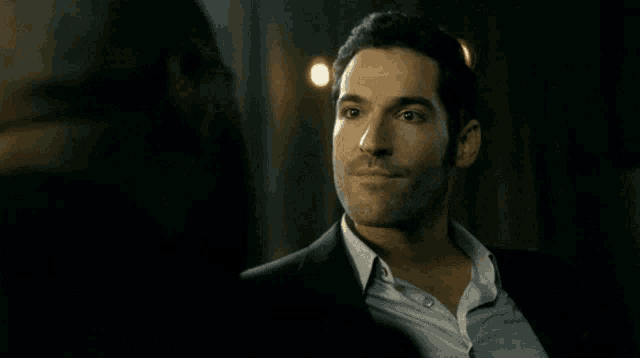 a man in a suit looks at another man in a dark room