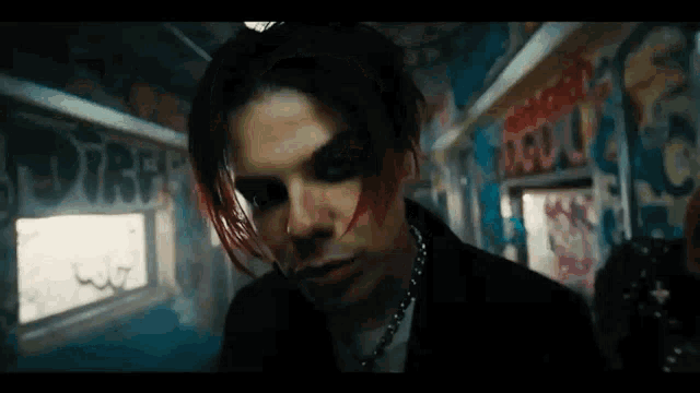 a man with red hair and black makeup is standing in a room with graffiti on the wall .