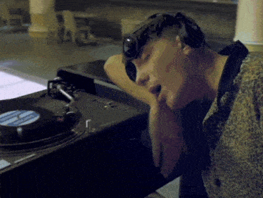 a man wearing headphones sits in front of a turntable that has a record on it