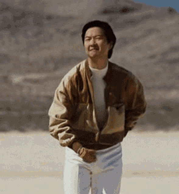 a man wearing a brown jacket and white pants stands in the desert