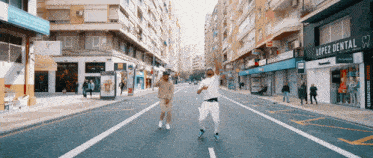 two men dancing on a street in front of a lopez dental sign