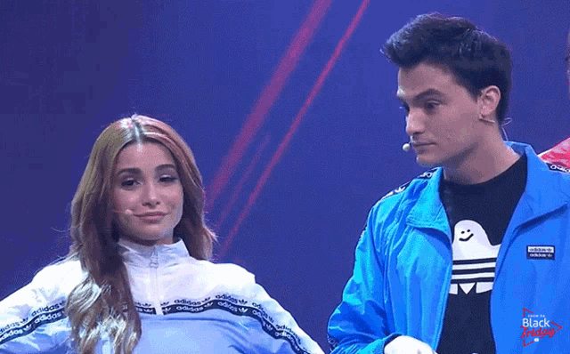 a man in a blue adidas jacket stands next to a woman in a white adidas jacket