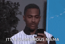 a man is holding a cell phone in his hand and saying `` it 's a glamorous mama '' .
