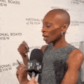 a woman is holding a microphone and talking into it while standing in front of a wall .