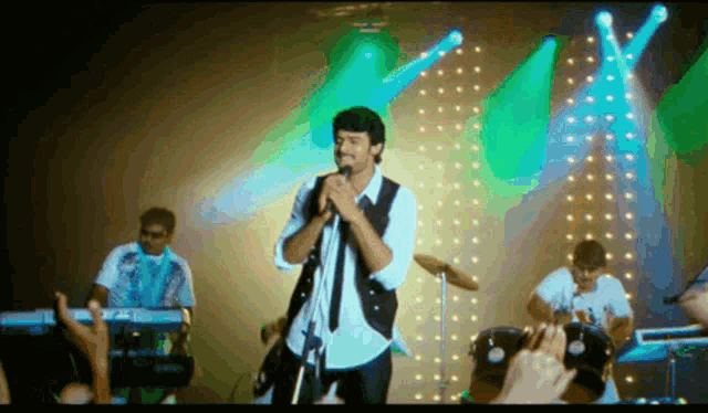 a man singing into a microphone on a stage with a band behind him