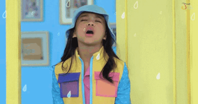a little girl wearing a blue hat and a yellow jacket is crying in the rain .