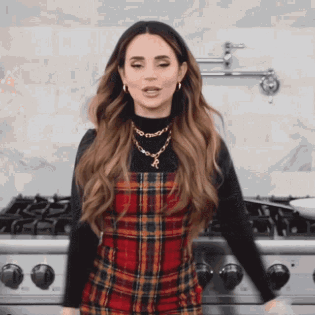 a woman wearing a plaid dress and a necklace with the letter r on it