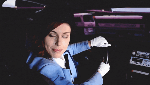 a woman in a blue uniform is sitting in a car with a pink bus behind her