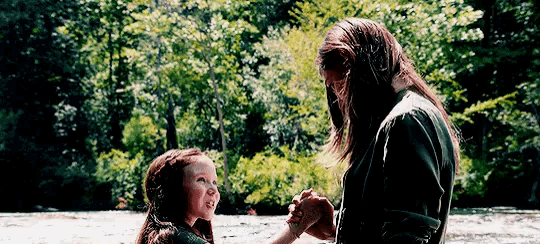 a man and a little girl are standing next to a river holding hands .