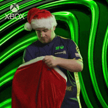 a man wearing a santa hat is holding a red item in front of a green background that says xbox
