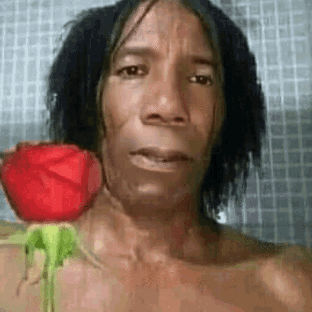 a man is holding a red rose in front of his face in a shower .