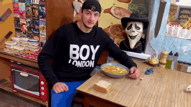 a man wearing a black boy london sweatshirt sits at a table