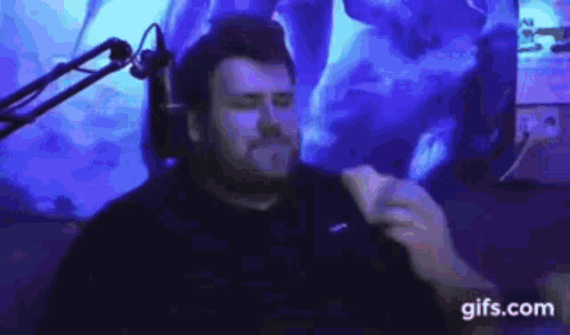 a man with a beard is sitting in front of a microphone and eating a sandwich .