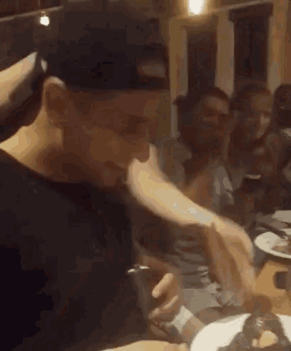 a man in a baseball cap is sitting at a table with a plate of food and looking at his phone .