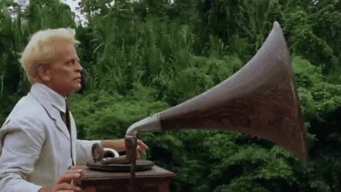 a man in a white suit is holding a phonograph in front of trees