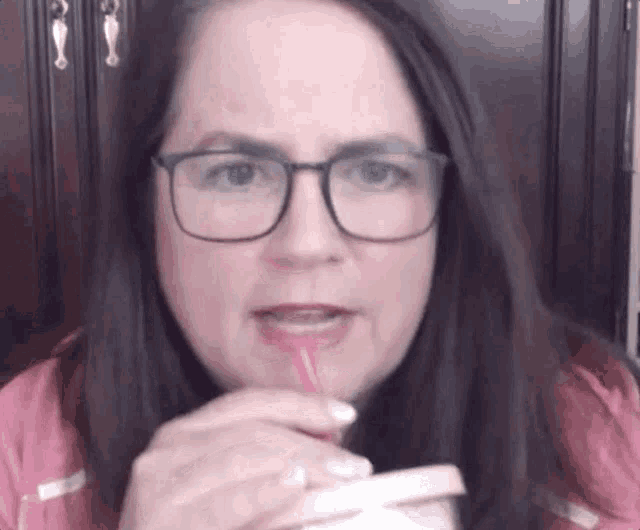 a woman wearing glasses is drinking through a straw from a cup .