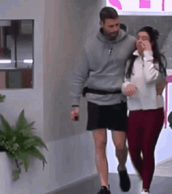 a man and a woman are walking down a hallway . the woman is covering her mouth with her hand .