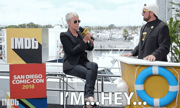 a woman sitting in front of a sign that says san diego comic-con 2018