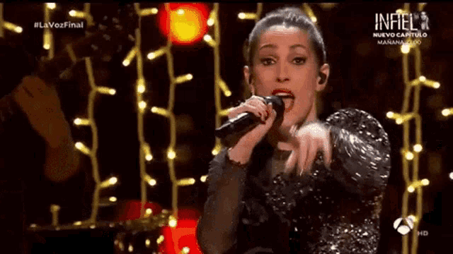 a woman is singing into a microphone on a stage in front of christmas lights .